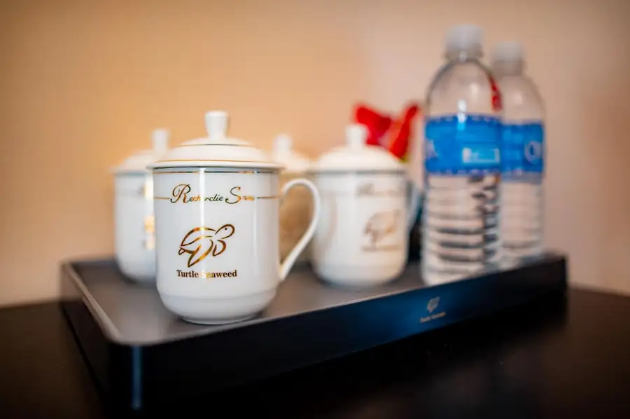 Complimentary bottled water and elegant porcelain mugs with gold turtle logos on a welcome tray in the Bedroom Deluxe Two Queen Beds at Turtle Seaweed Resort.